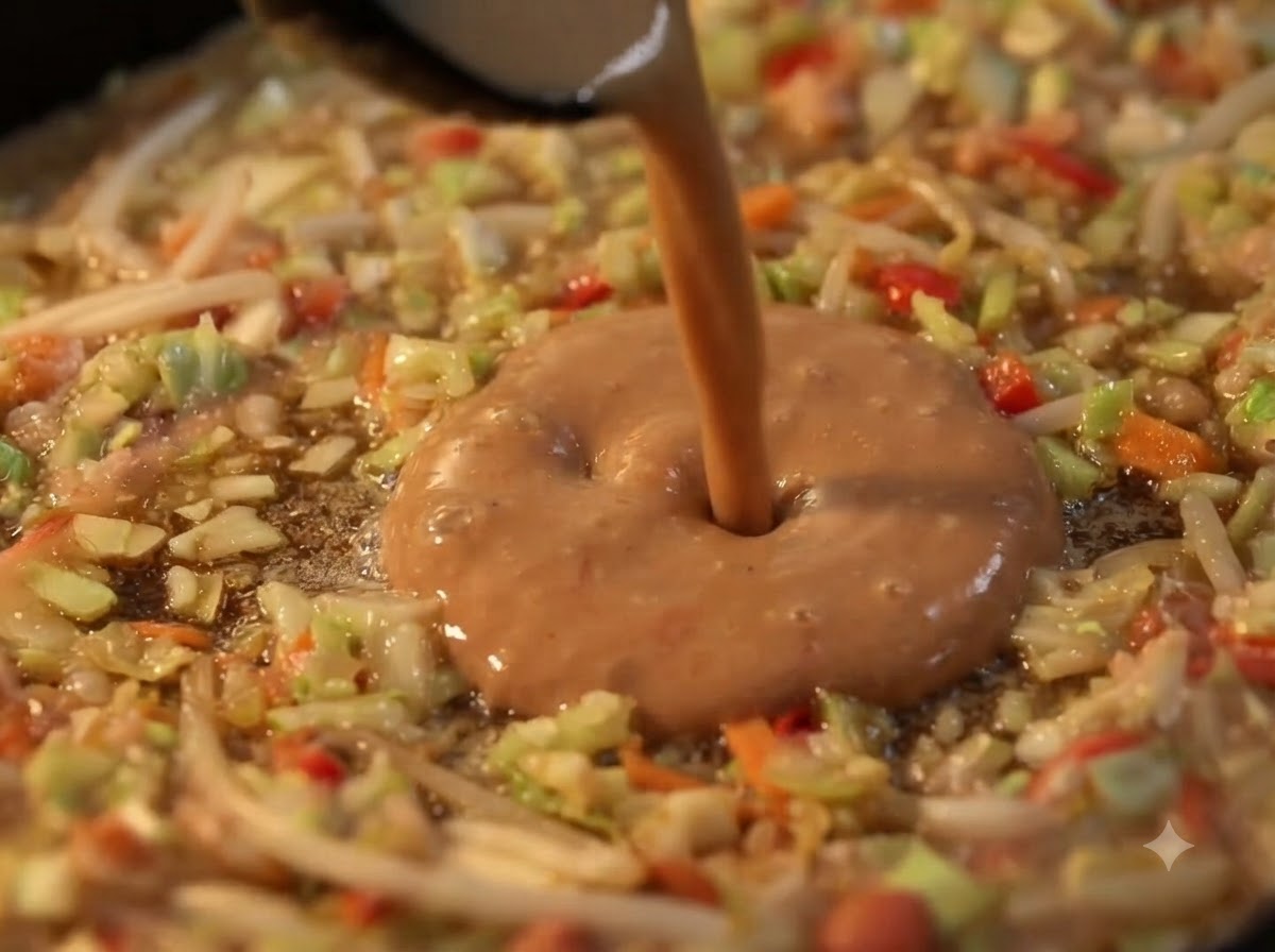 De la pâte liquide versée dans le centre creux dun anneau de légumes sur une plaque chauffante.