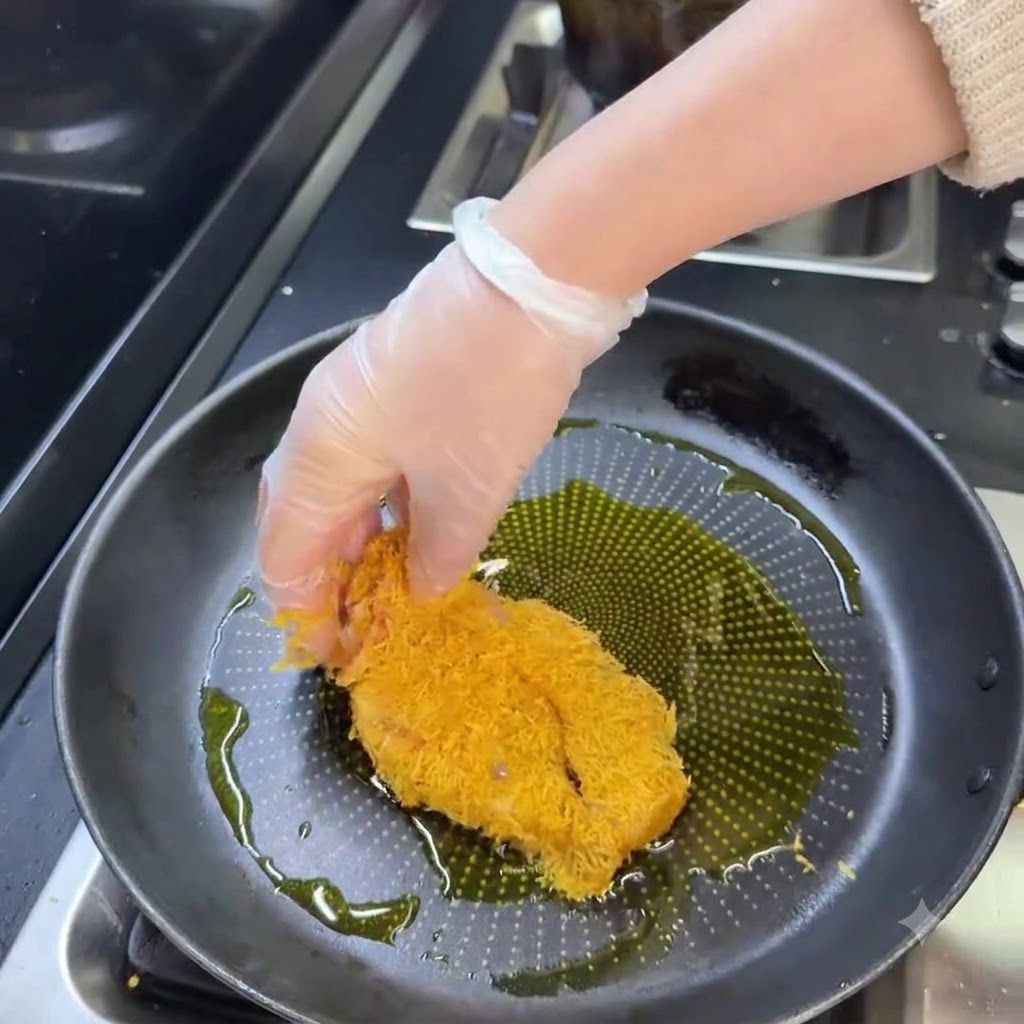 Une escalope de porc panée en train de frire dans une poêle remplie dhuile chaude jusquà devenir dorée.