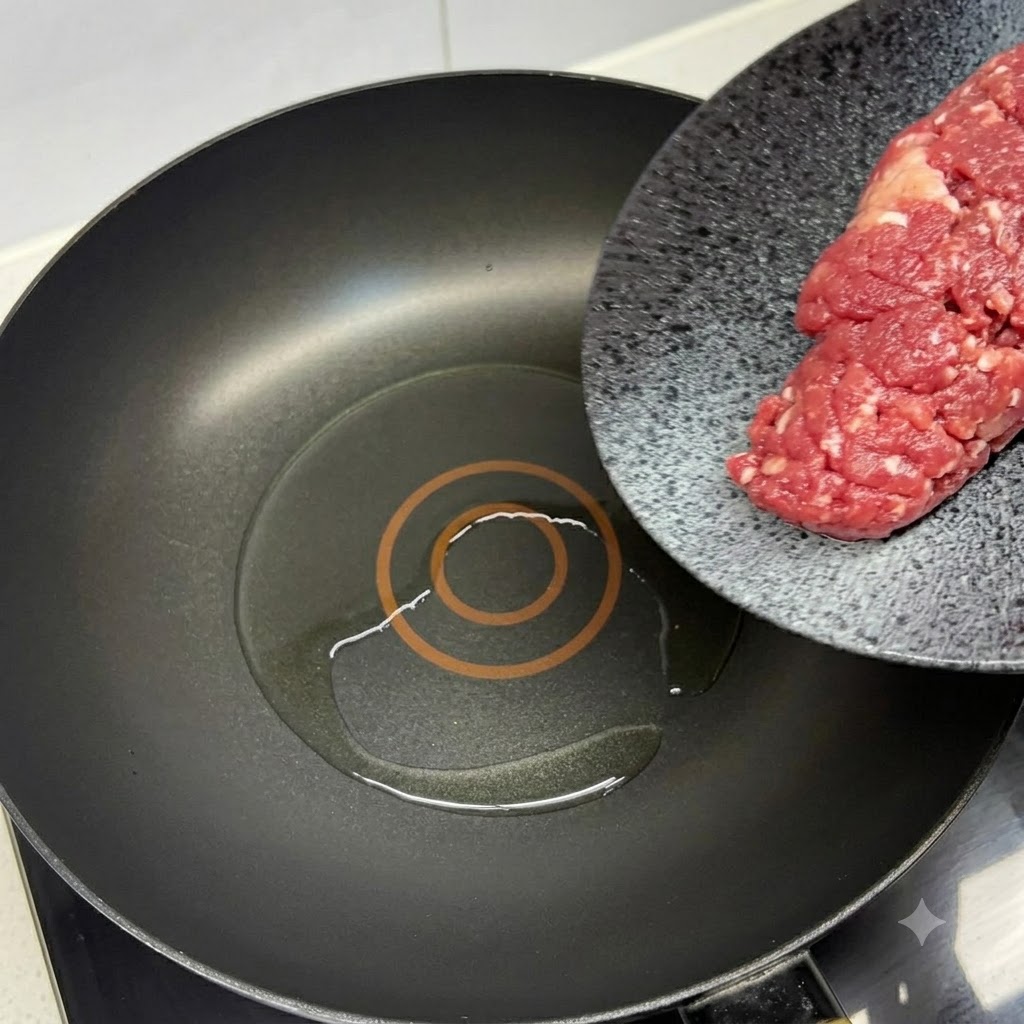 Bœuf haché frais ajouté dans une poêle noire chaude huilée avec une spatule rouge.