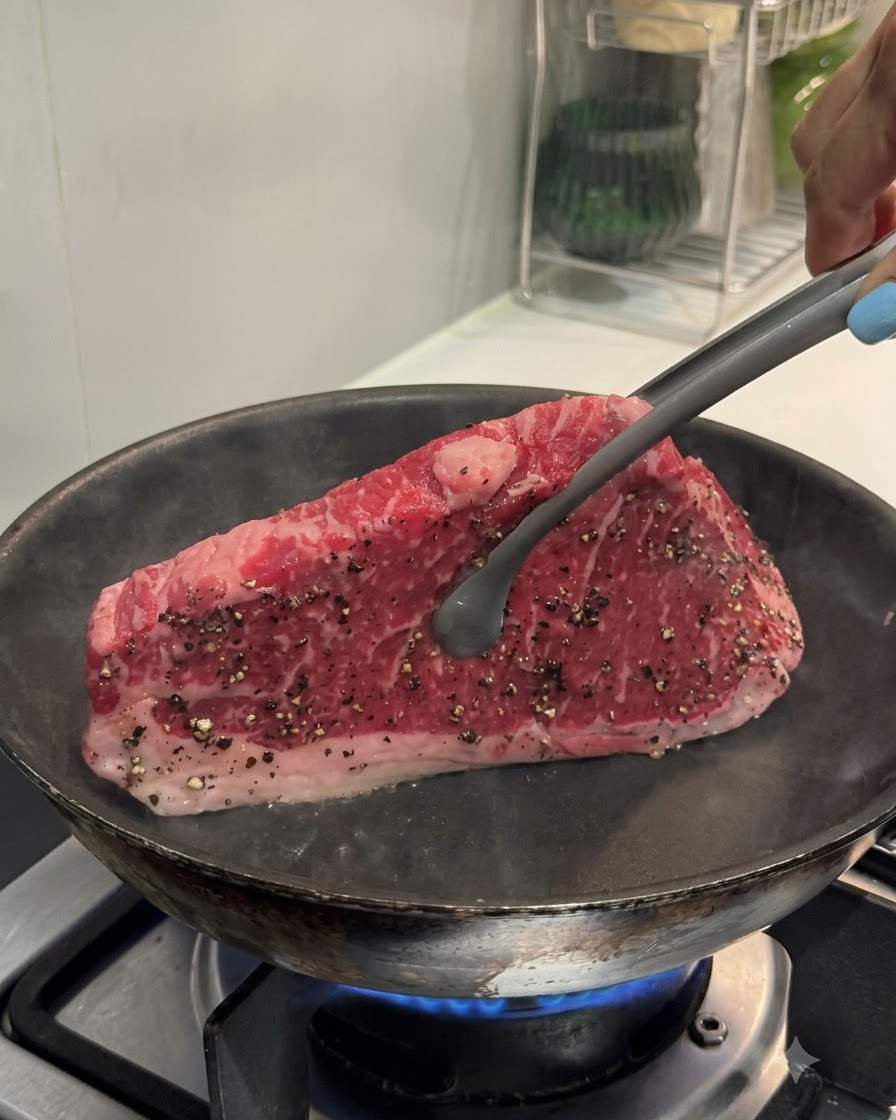 Une pince tenant un steak bien droit contre une poêle chaude pour saisir le bord.