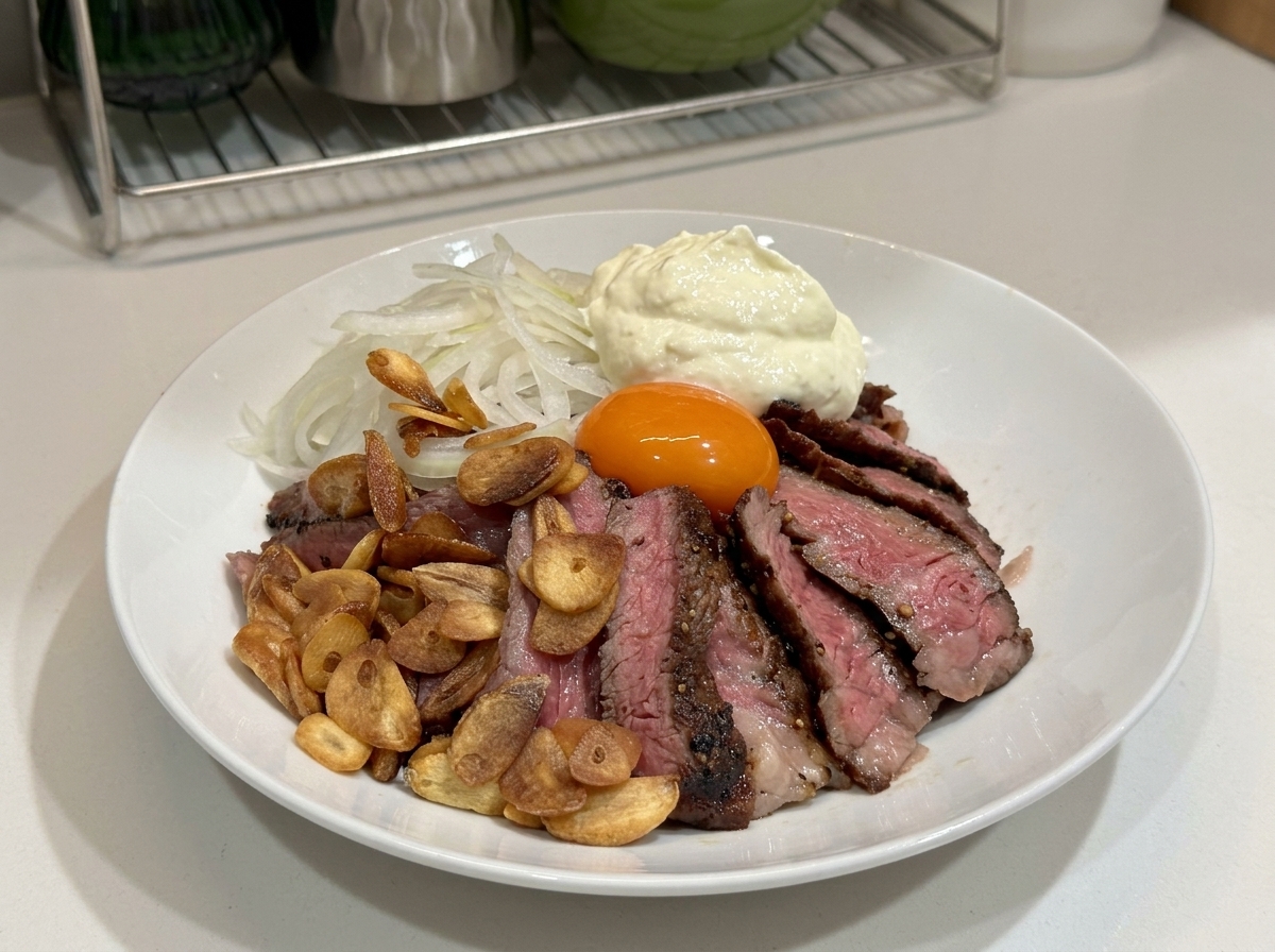 Un bol blanc rempli de steak tranché, de chips dail, doignons, dun jaune dœuf et dune grande cuillère de crème fouettée sur le dessus.