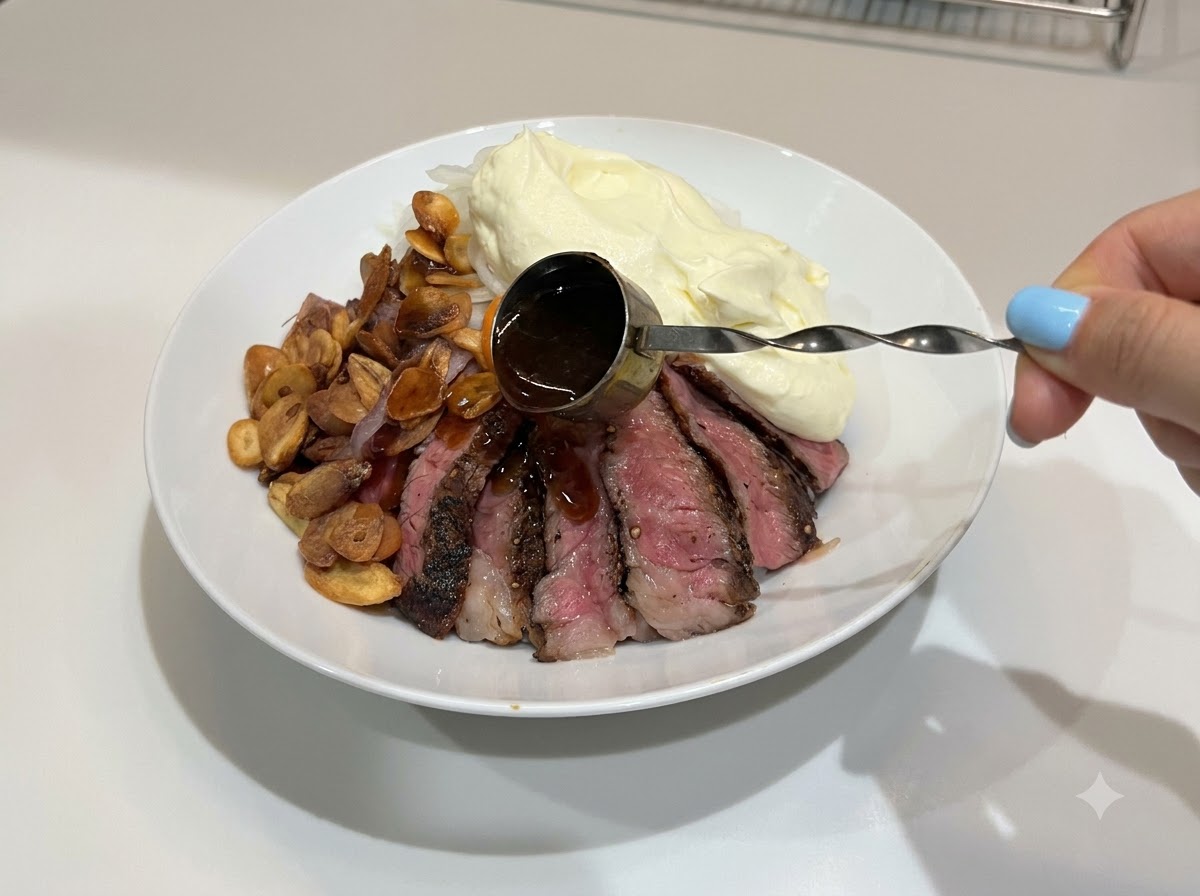 Une main utilisant une petite mesure à manche pour verser de la sauce teriyaki foncée et brillante sur un bol de riz au steak complété.