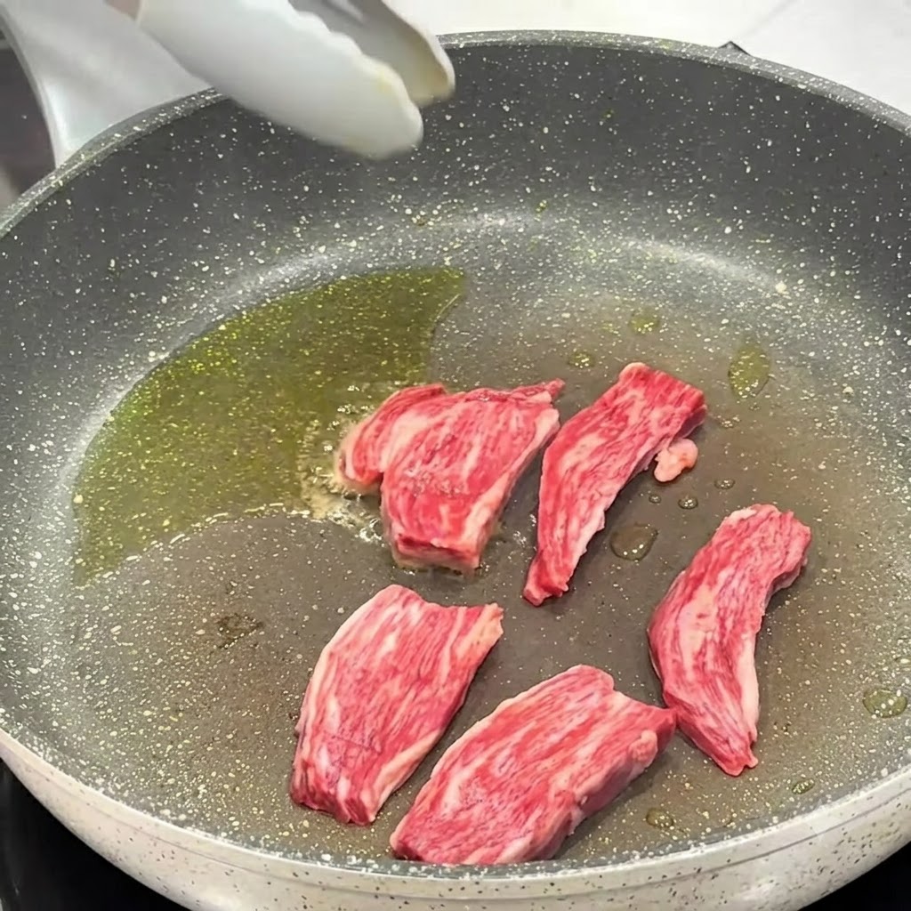 Sel et poivre noir saupoudrés sur les morceaux de steak en cours de cuisson dans la poêle.