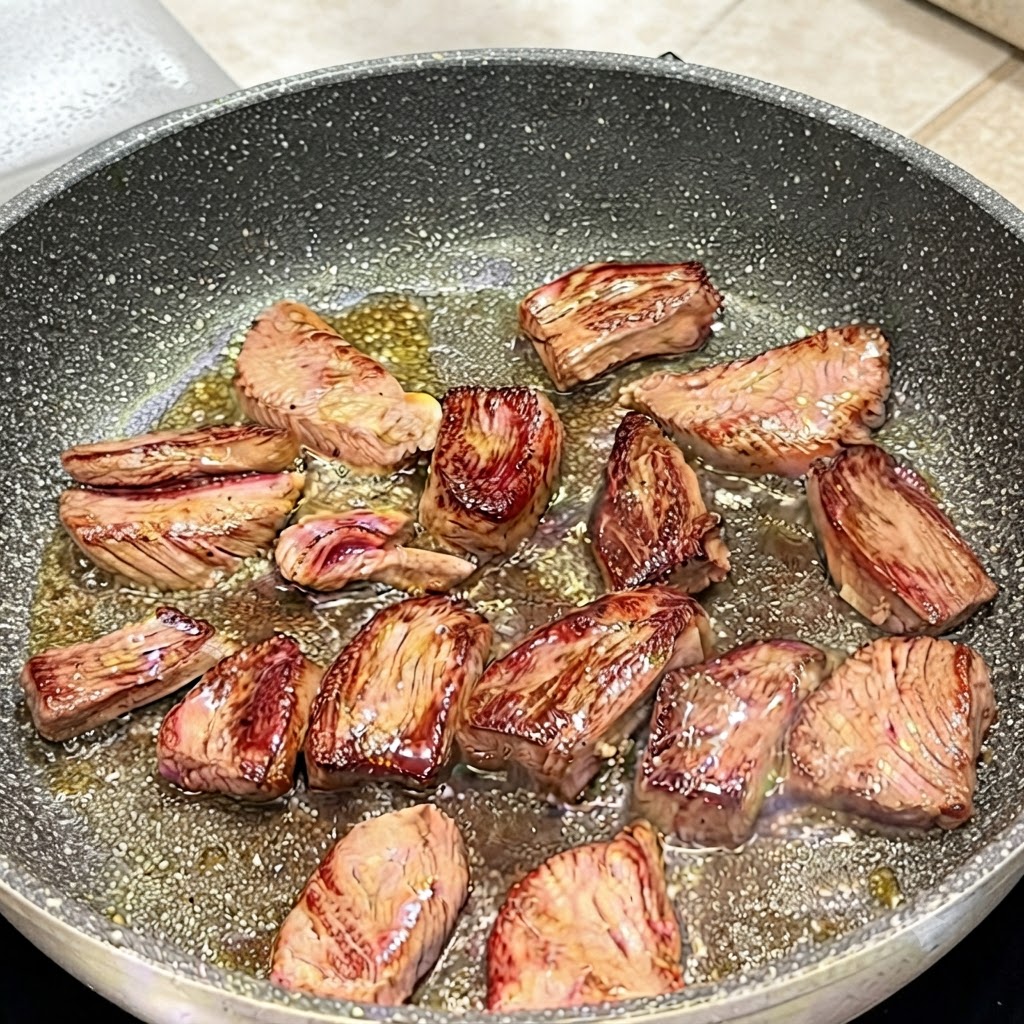 Pinces retournant des morceaux de bavette dans une poêle pour montrer les surfaces dorées.