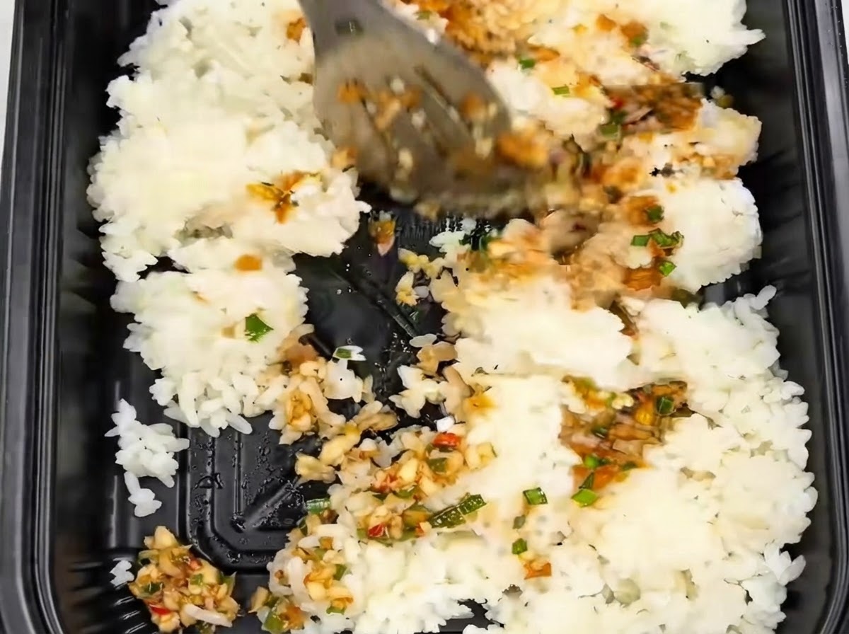 Riz remué et mélangé avec des pinces à lintérieur dun récipient noir à emporter aux côtés de la sauce à lail.