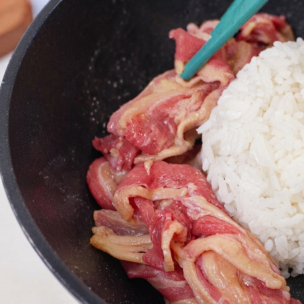 Tranches de bœuf cru disposées en anneau autour du monticule de riz dans la poêle.