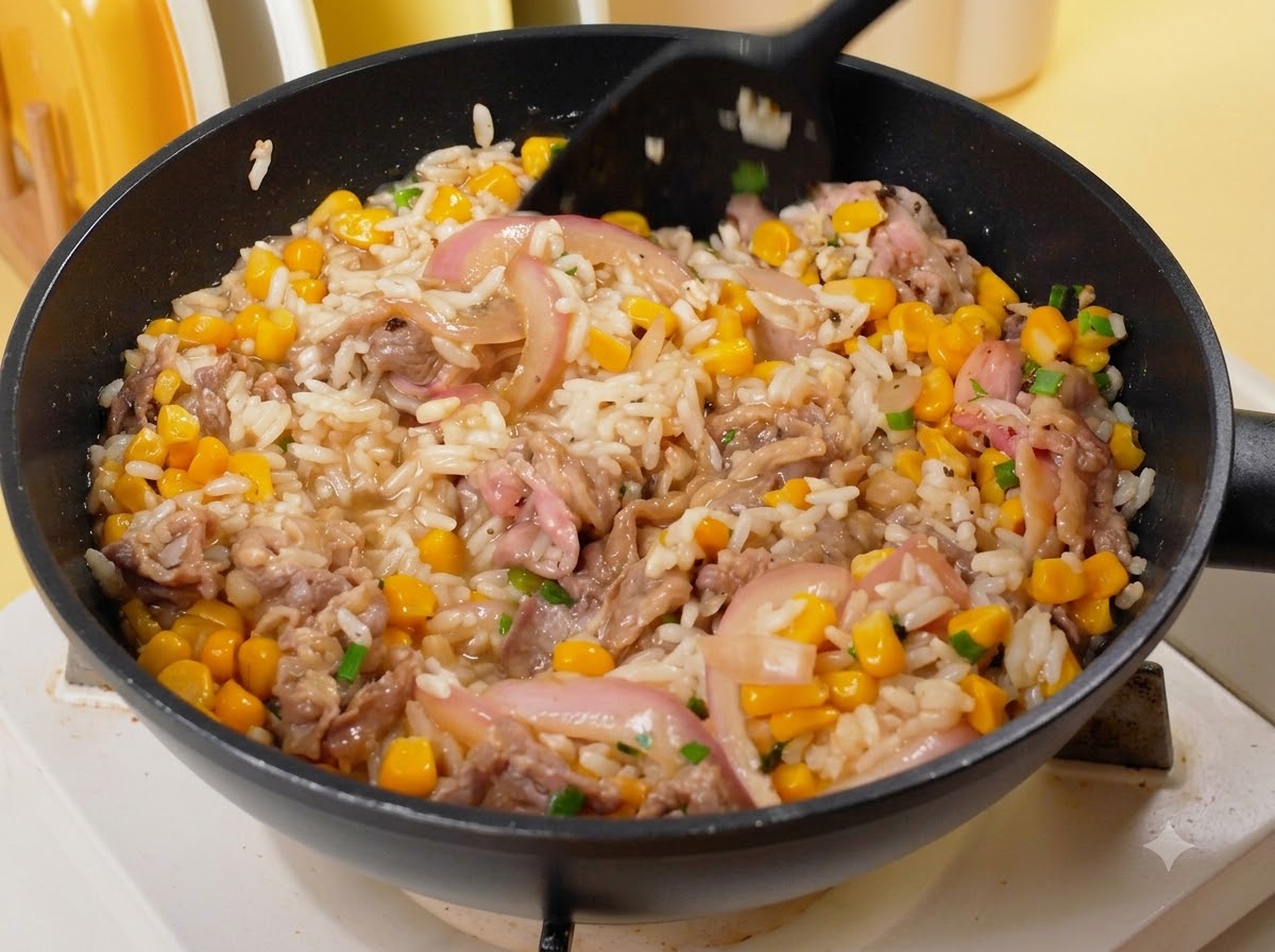 Une spatule noire mélangeant le riz, le bœuf, le maïs et les oignons ensemble dans une poêle sur le feu.