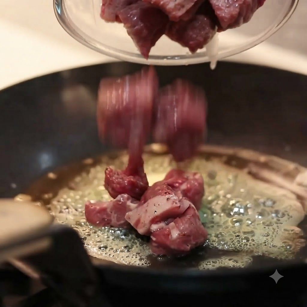 Morceaux de bœuf cru assaisonnés versés dun bol en verre dans une poêle chaude à fond plat remplie de beurre fondu bouillonnant.