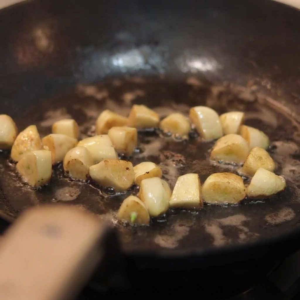 Champignons blancs émincés jetés dans une poêle contenant des gousses dail dorées sautées.