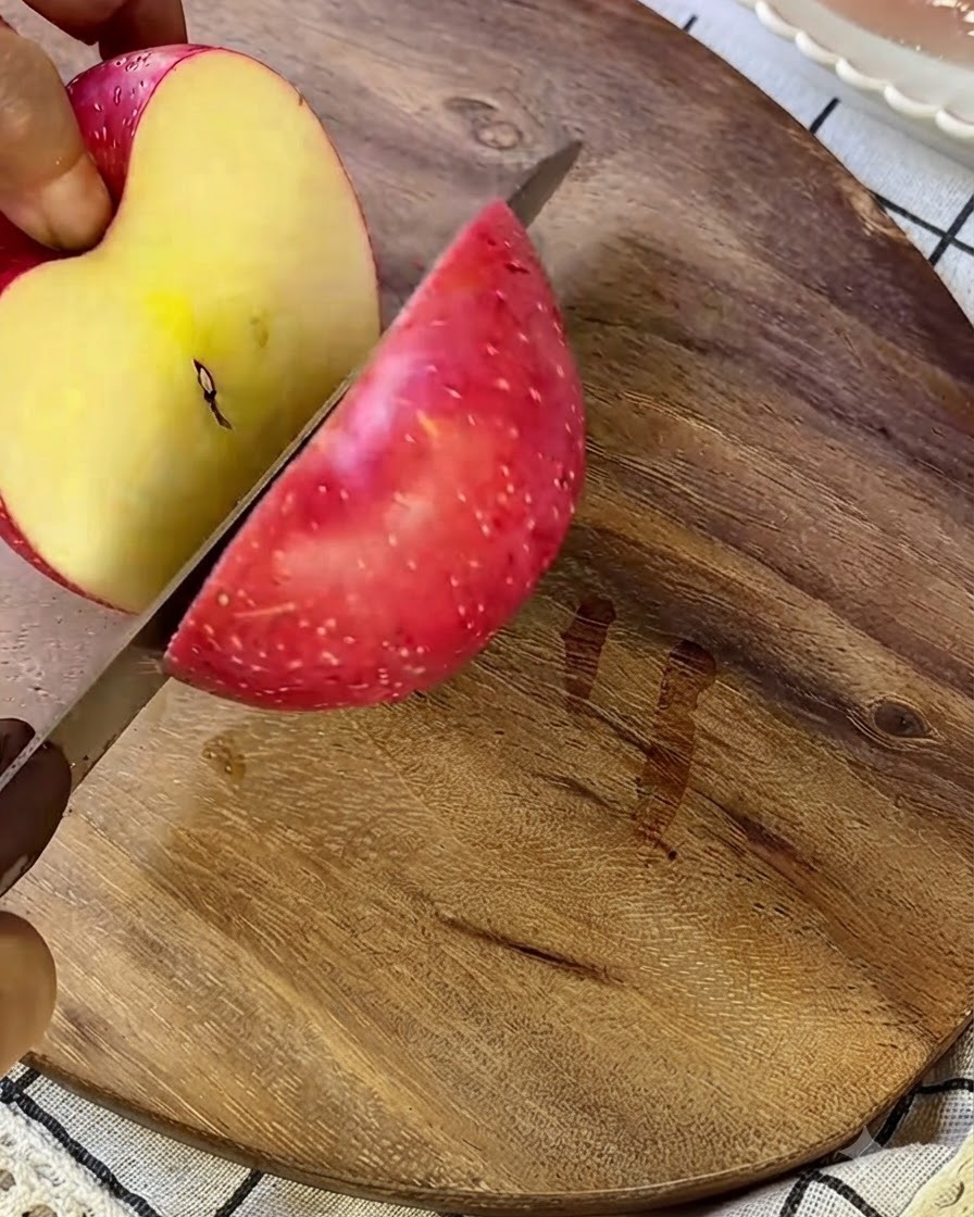 Une pomme coupée en petits morceaux sur une planche à découper en bois avec un couteau argenté.