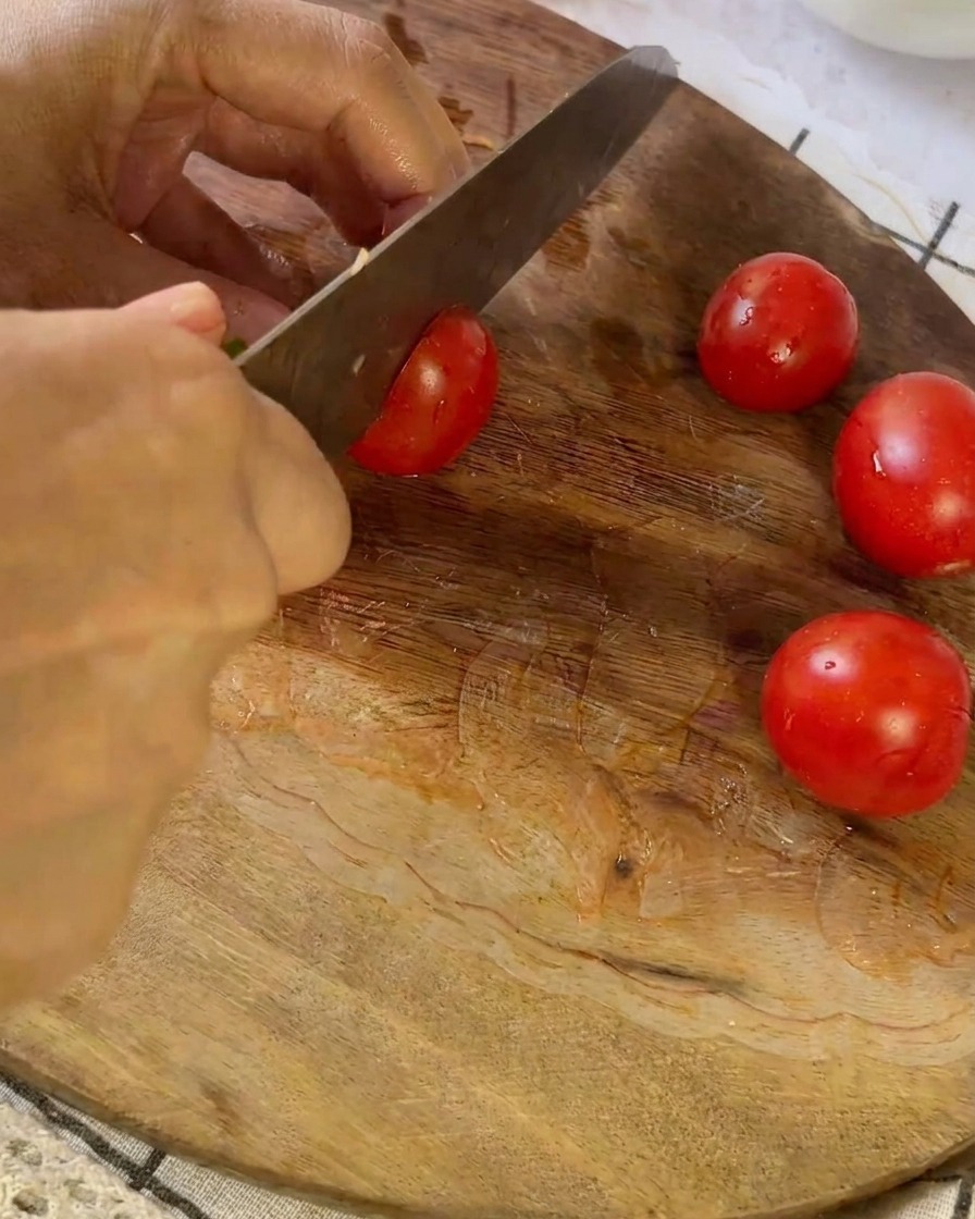 Un couteau coupant une petite tomate rouge sur une planche à découper en bois à côté dautres tomates coupées en deux.
