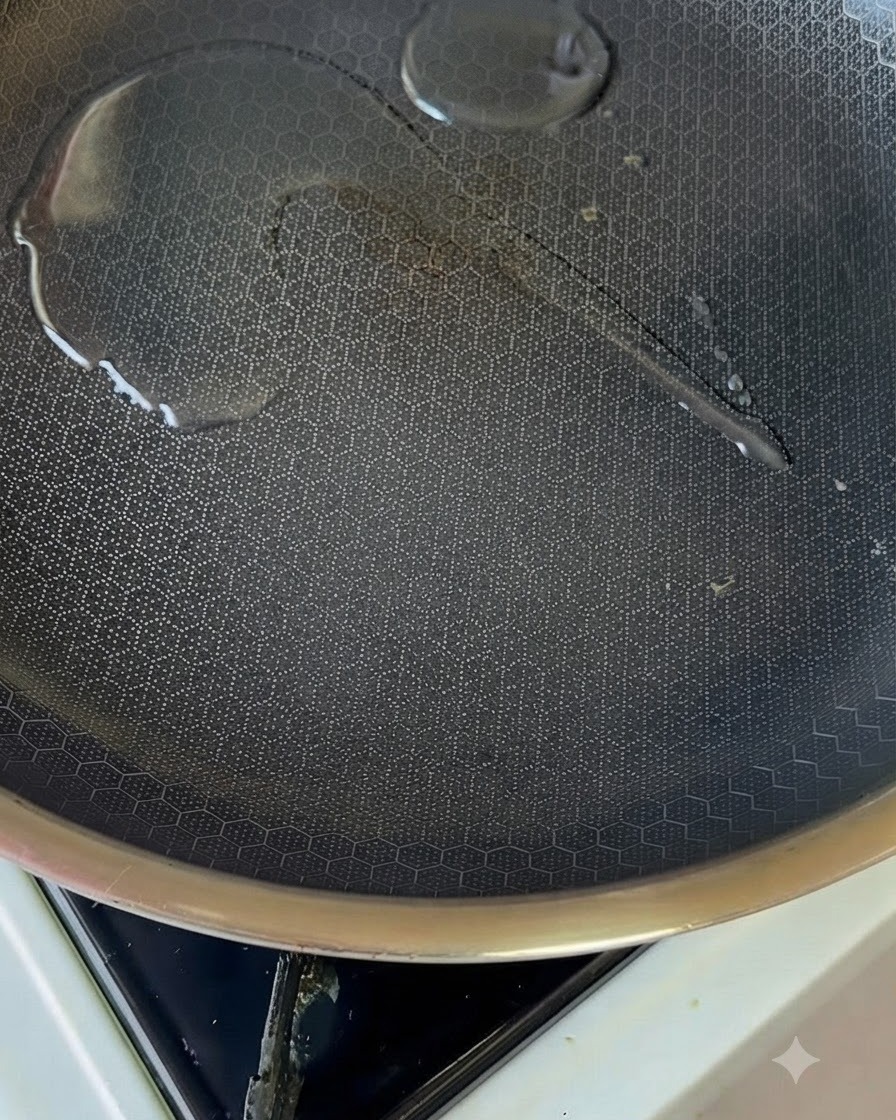 Une petite quantité dhuile brillante à lintérieur dune poêle antiadhésive chauffée sur un brûleur de cuisinière.