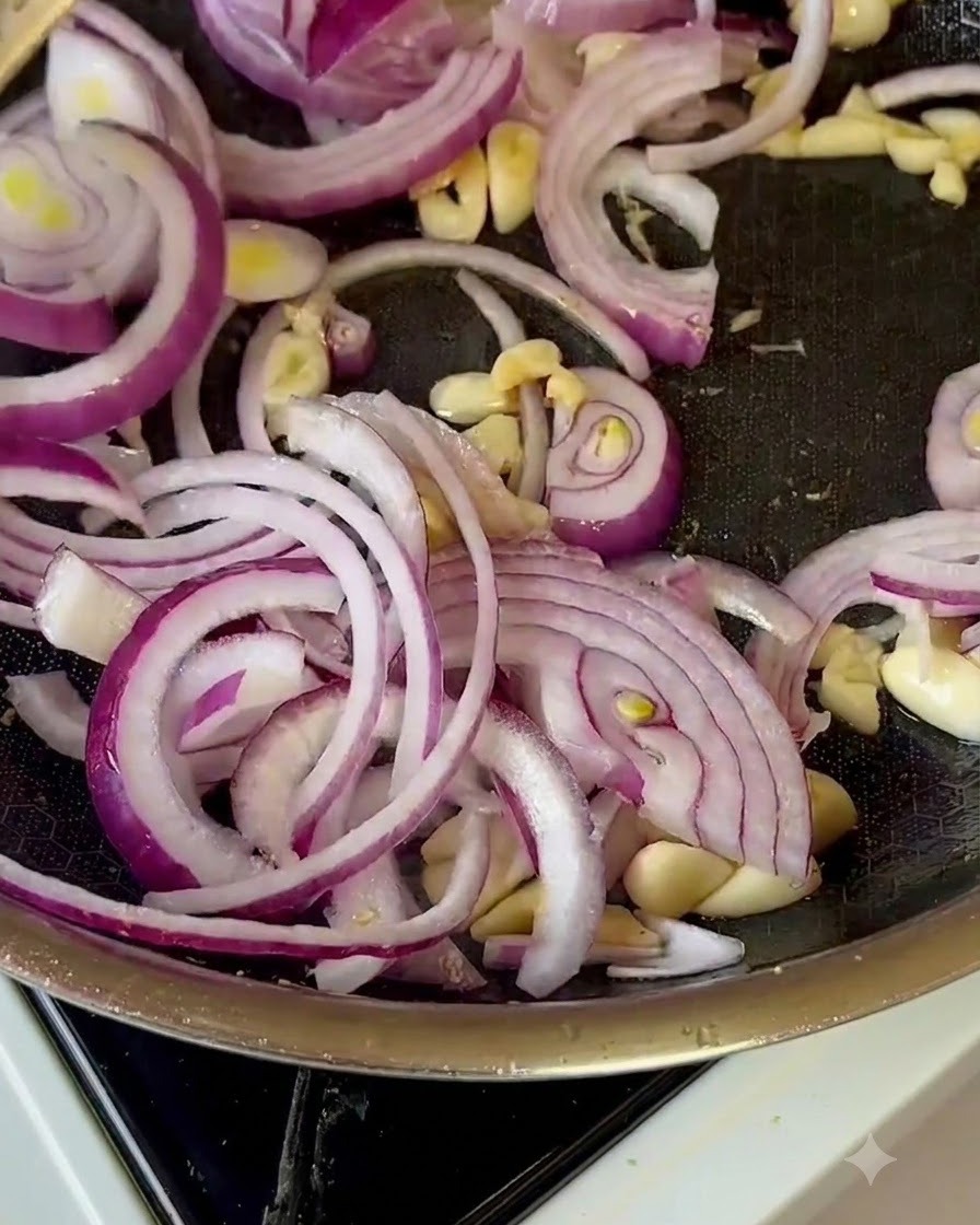 Des tranches doignons rouges, de lail et des morceaux de pommes mélangés dans une poêle à frire.