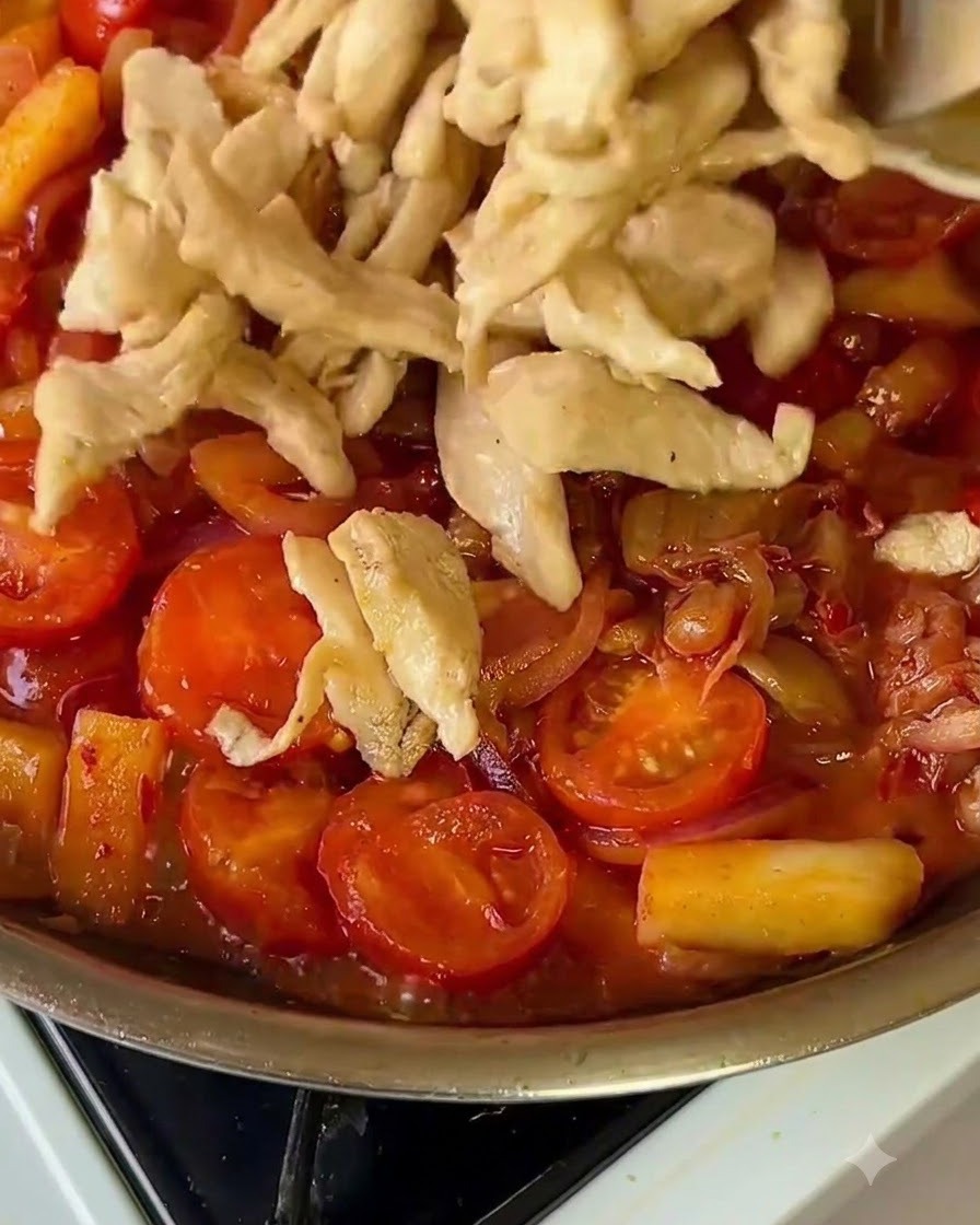 Des lanières de poulet cuit remises dans une poêle colorée de légumes.