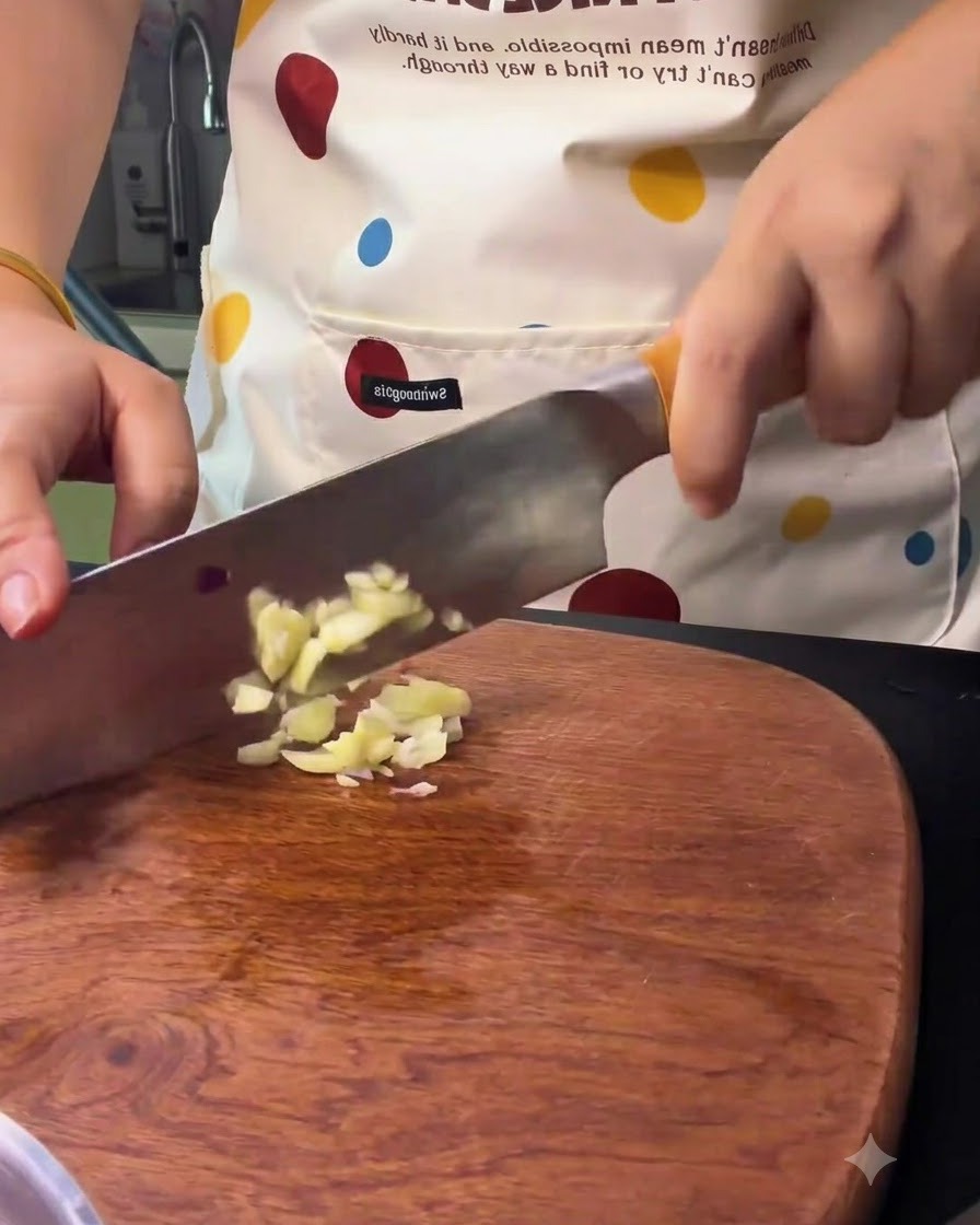 Des gousses dail en train dêtre coupées et émincées avec un couteau de cuisine sur une planche en bois.