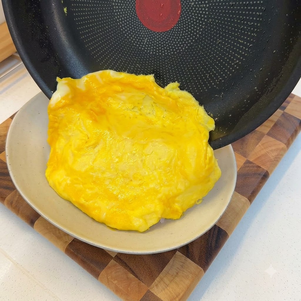 Une omelette cuite et moelleuse glissant hors dune poêle et se drapant sur une portion de riz blanc.