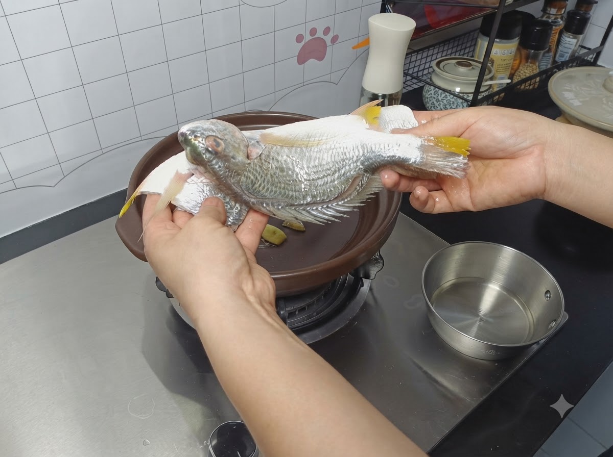 Un poisson entier assaisonné placé dans une cocotte sur des tranches de gingembre.