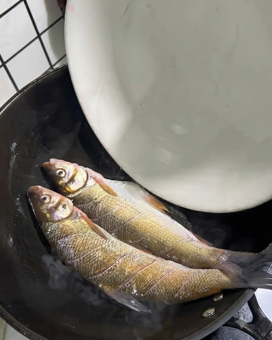 Deux poissons queue jaune entiers placés dans un wok chaud avec de lhuile.