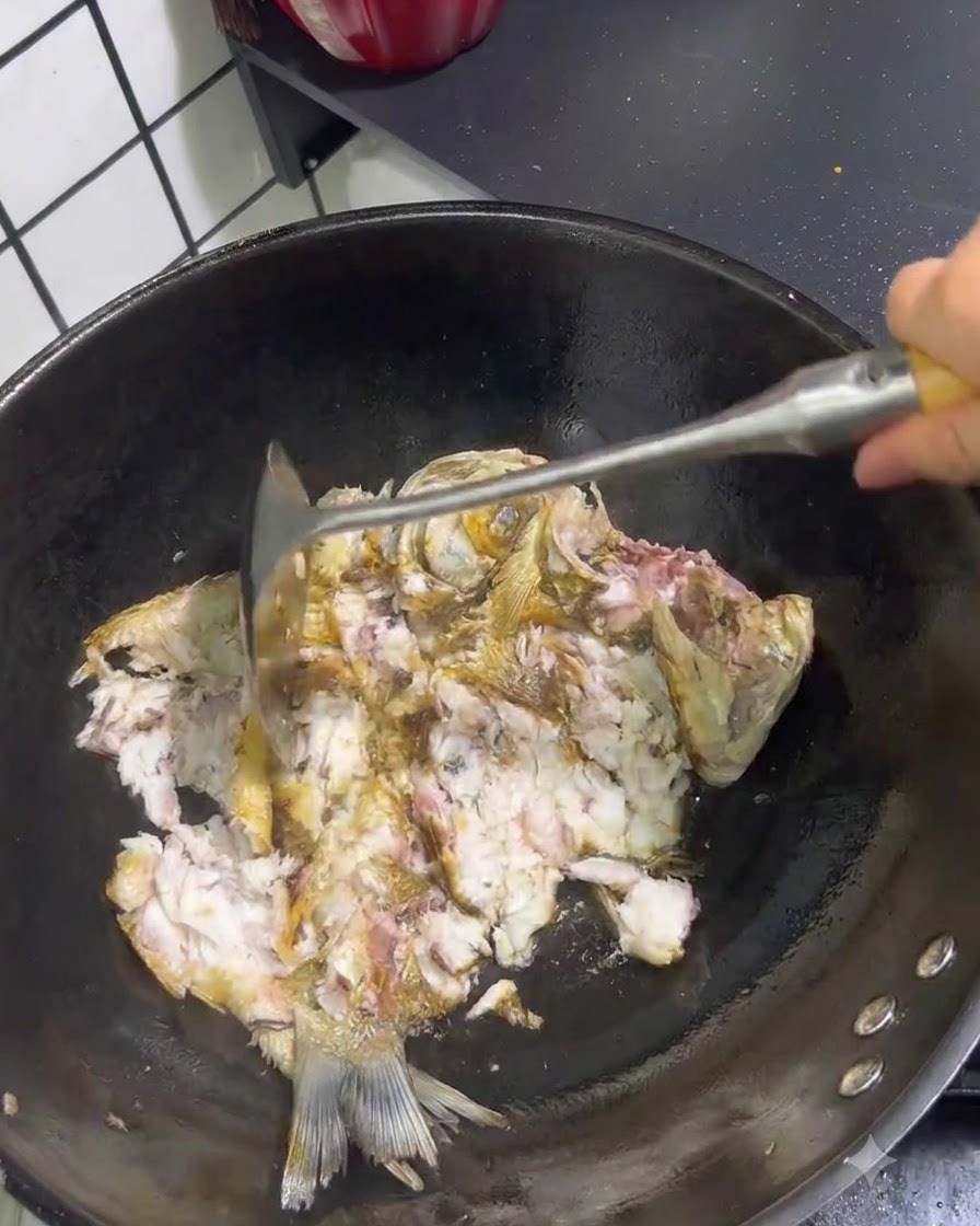 Poisson frit en train dêtre brisé et écrasé avec une spatule en métal à lintérieur dun wok.