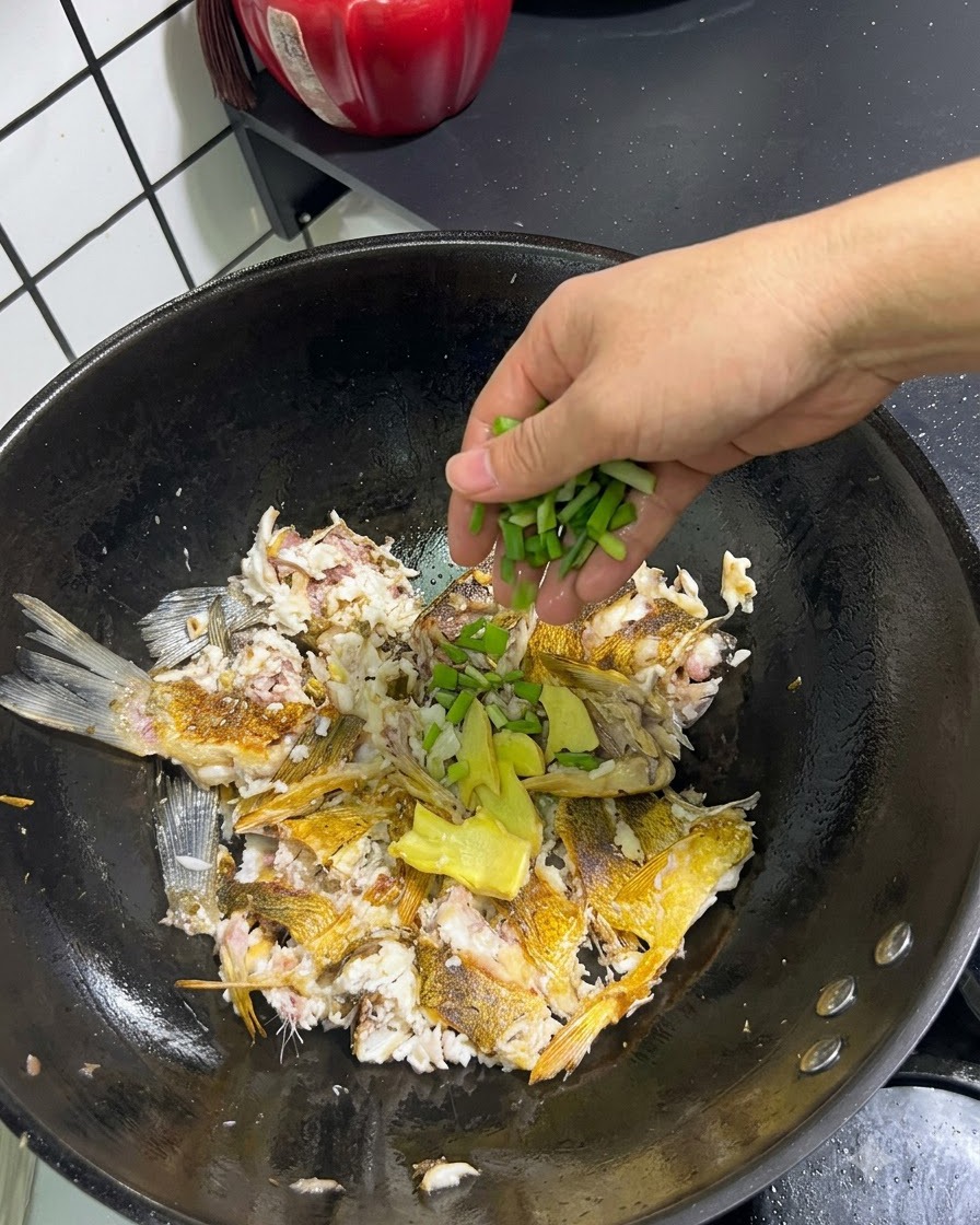 Oignons verts frais et gingembre tranché ajoutés à la main sur le poisson écrasé dans un wok.
