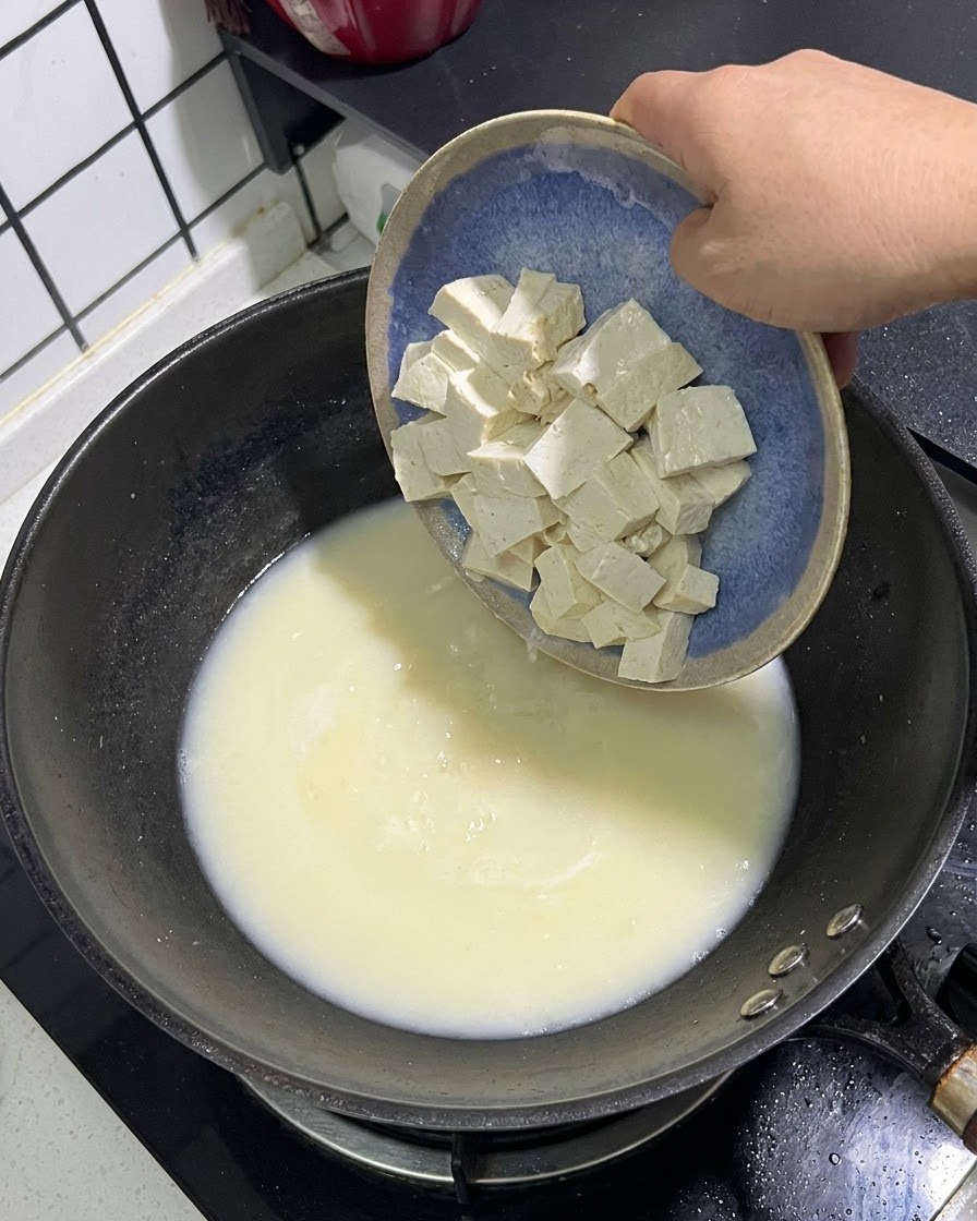 Cubes de tofu blanc glissant dune assiette bleue dans une casserole de bouillon de poisson blanc crémeux.