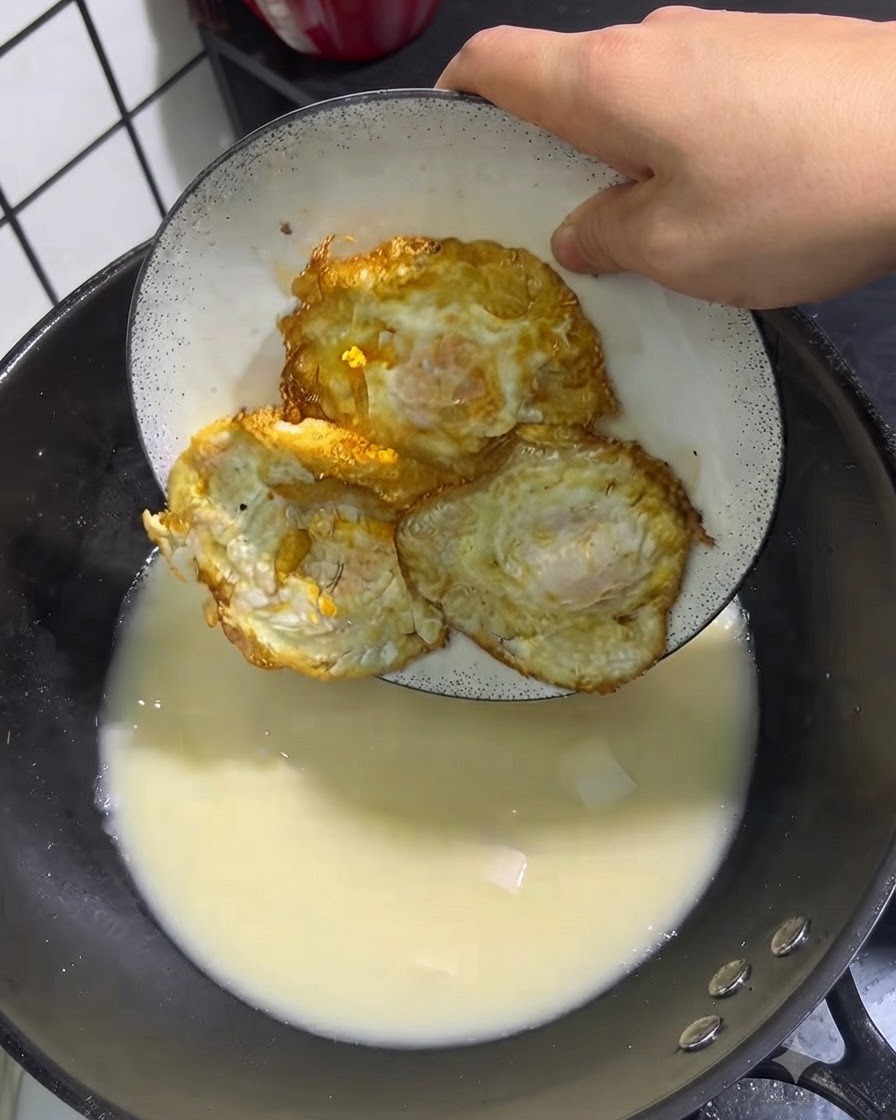 Trois œufs frits dorés placés dune assiette blanche dans une casserole de soupe frémissante.