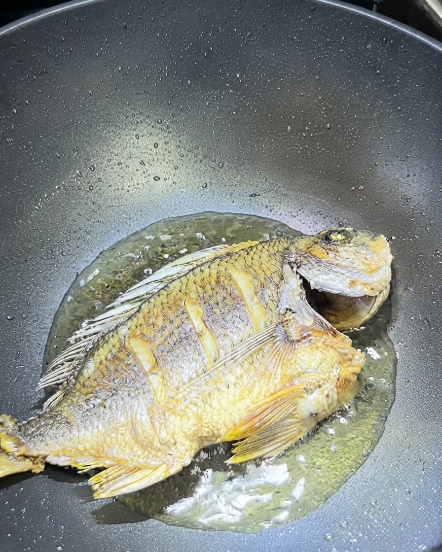 Gingembre tranché et ail éparpillés autour du poisson frit dans un wok.