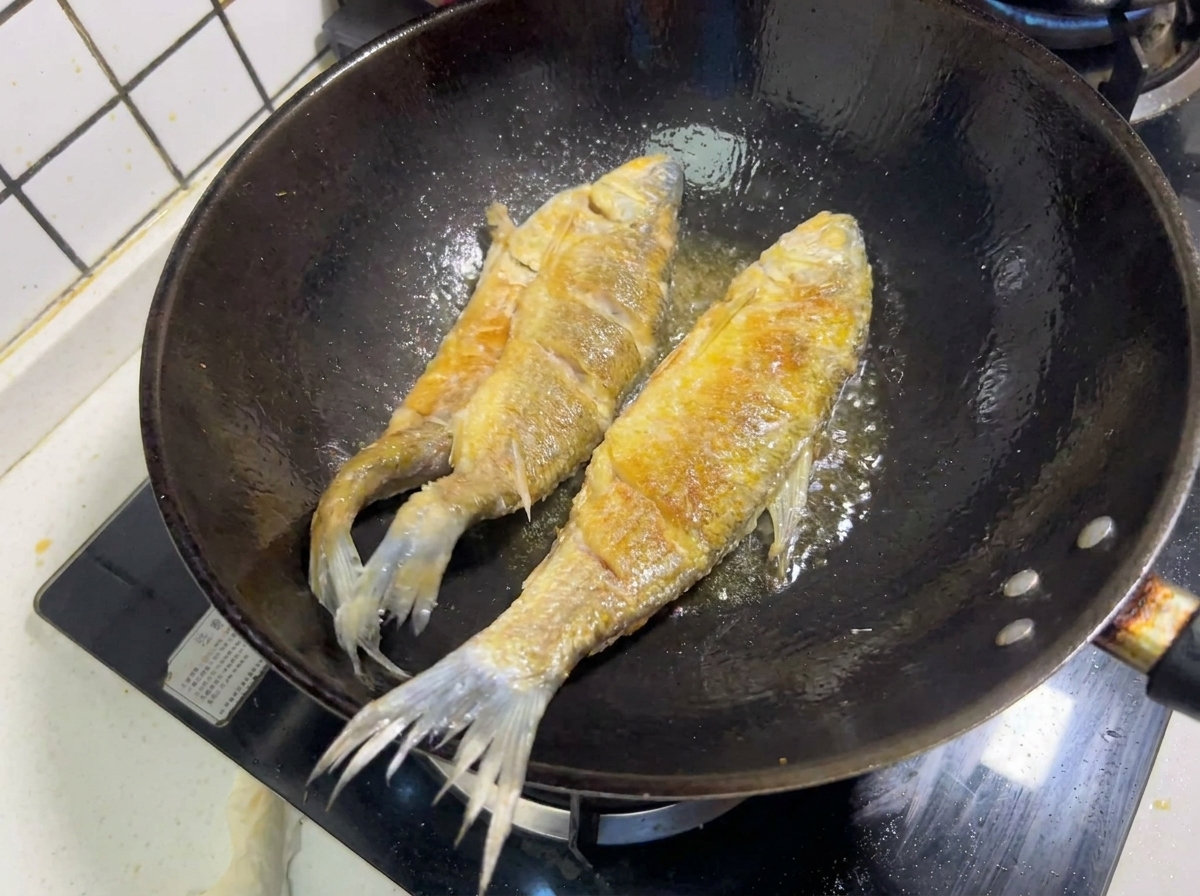 Deux poissons entiers en train de frire dans lhuile chaude dun wok, affichant une croûte dorée.