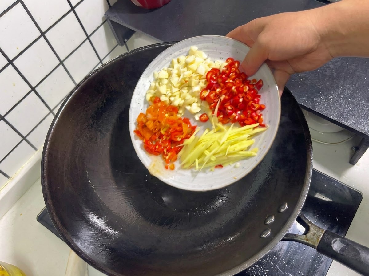 Ail émincé, piments rouges, piments marinés et lamelles de gingembre jetés dans un wok.