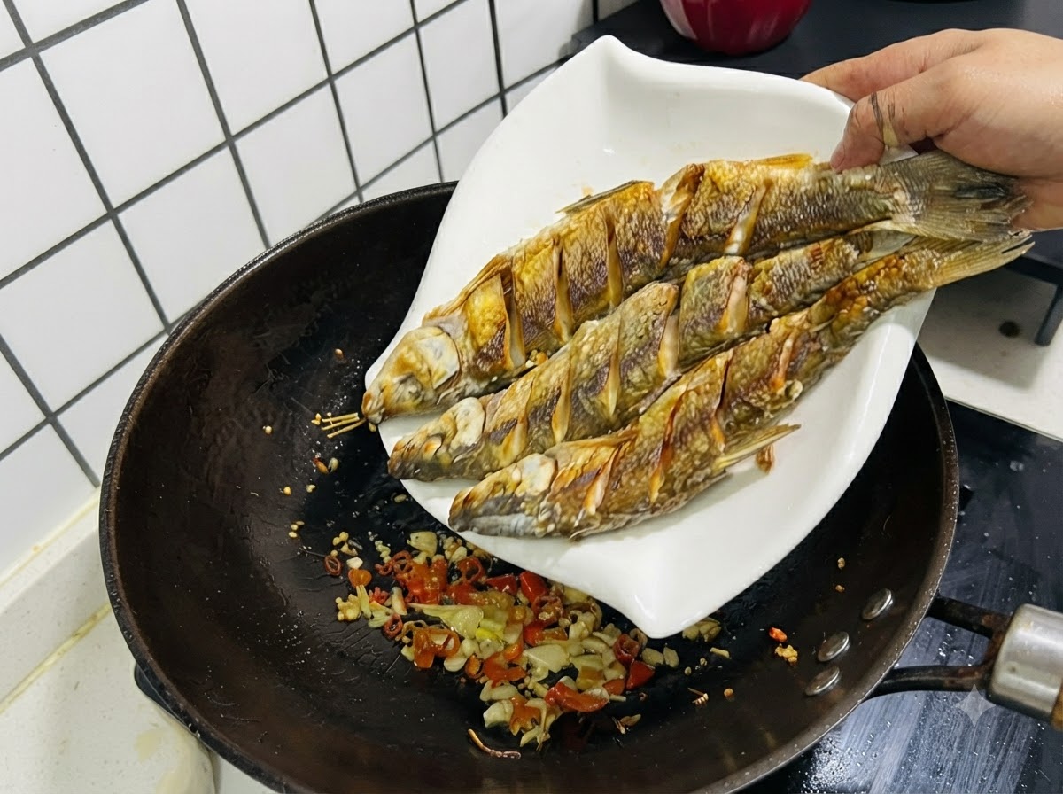 Trois poissons frits glissant dune assiette blanche pour retourner dans le wok contenant lail, le gingembre et les piments sautés.