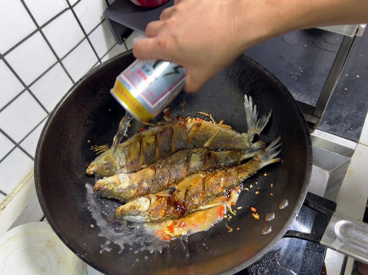 Une main versant une canette de bière dans un wok sur le poisson frit assaisonné et les aromates sautés.