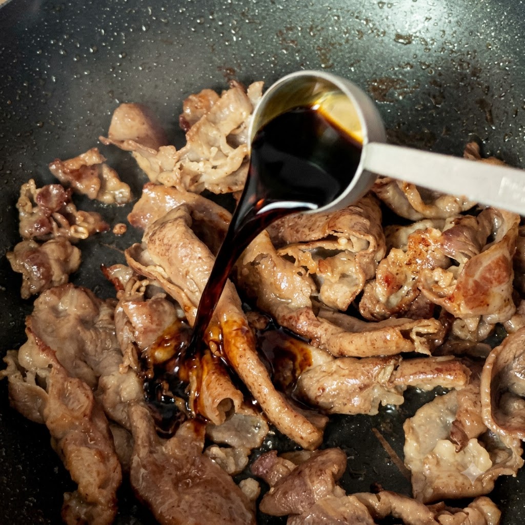 Une cuillère de mesure versant de la sauce soja claire sur des tranches de bœuf cuites dans une poêle.