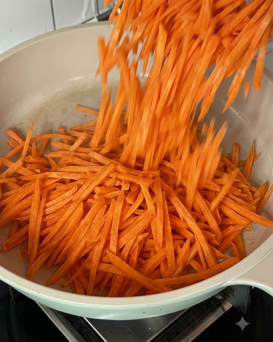 Carottes râpées fraîches en train dêtre mélangées et sautées dans une poêle chaude.