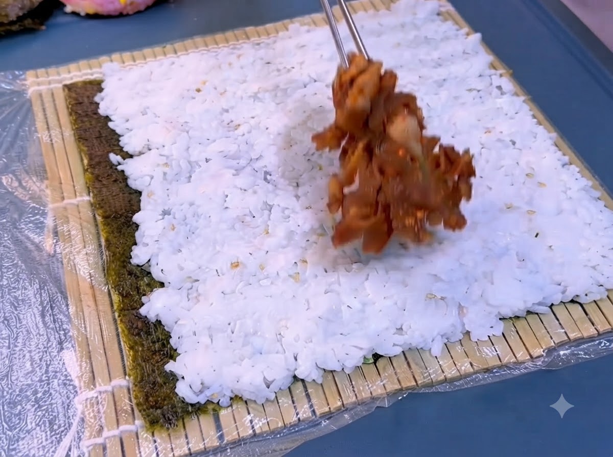 Une feuille dalgue foncée sur une natte en bambou recouverte dune couche de riz blanc en cours détalement.