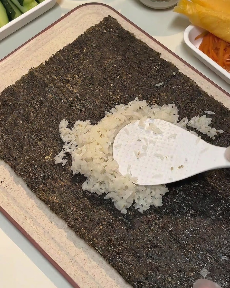 Une palette à riz blanche étalant du riz assaisonné au centre dune feuille dalgue.