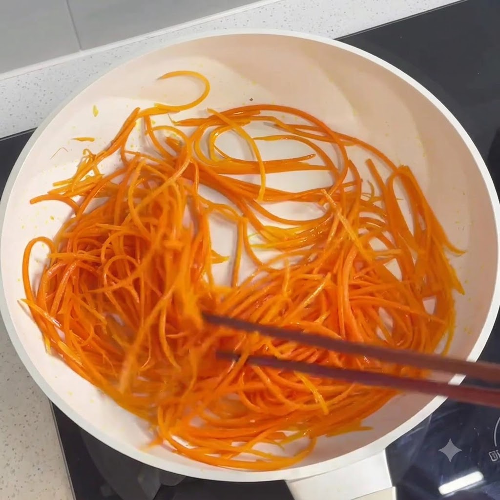 Carottes râpées en train dêtre mélangées et cuites dans une poêle à laide de baguettes.