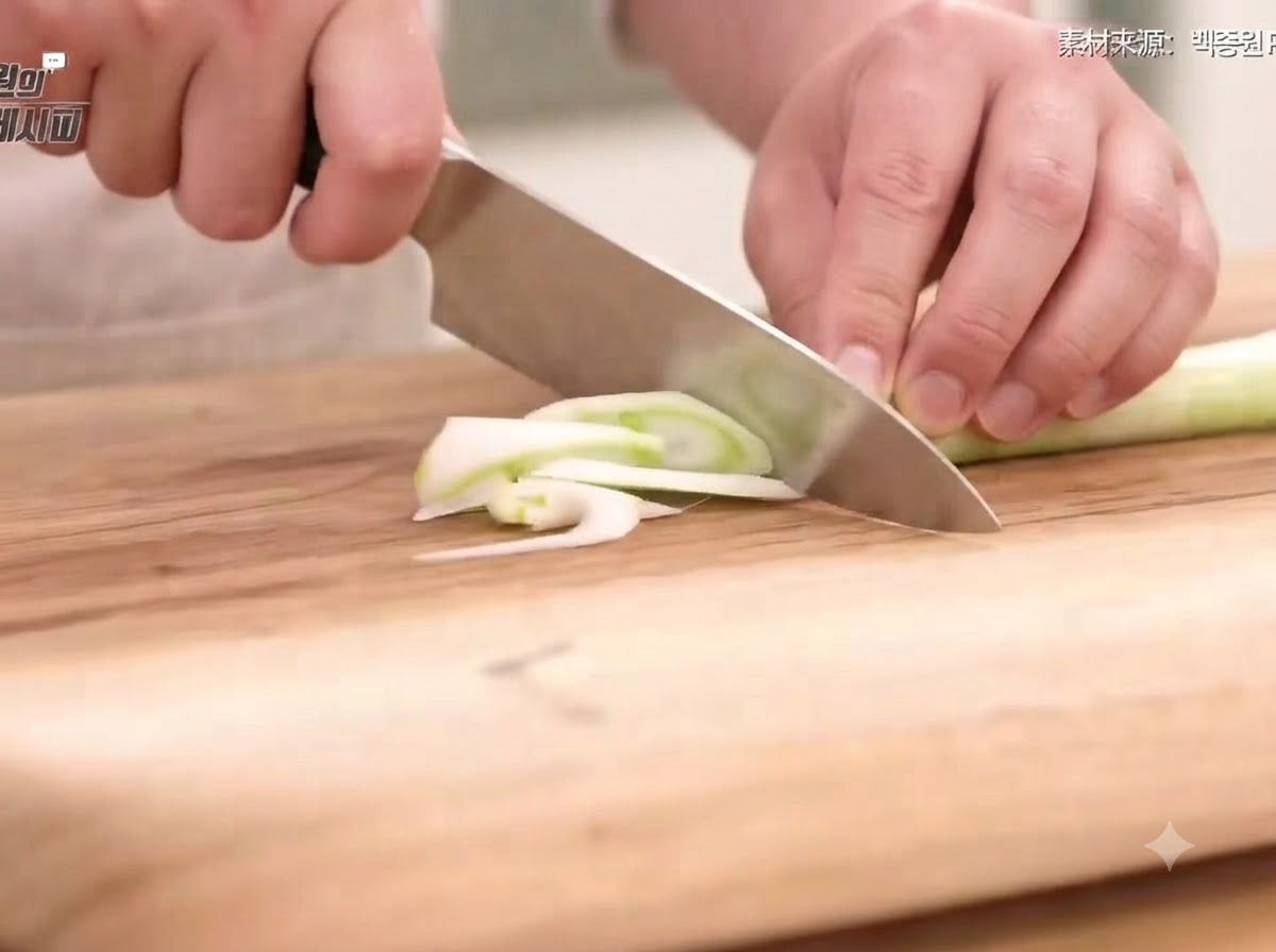 Oignon vert, oignon, carotte et piments coupés en fines tranches et lanières sur une planche à découper en bois avec un couteau.