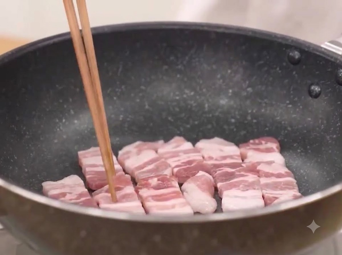 Tranches de poitrine de porc en train de frire dans une poêle chaude en grésillant.