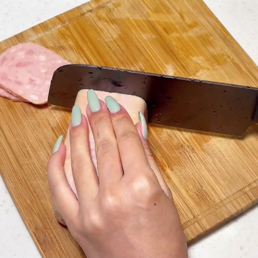 Du luncheon meat coupé uniformément sur une planche en bois avec un couteau.
