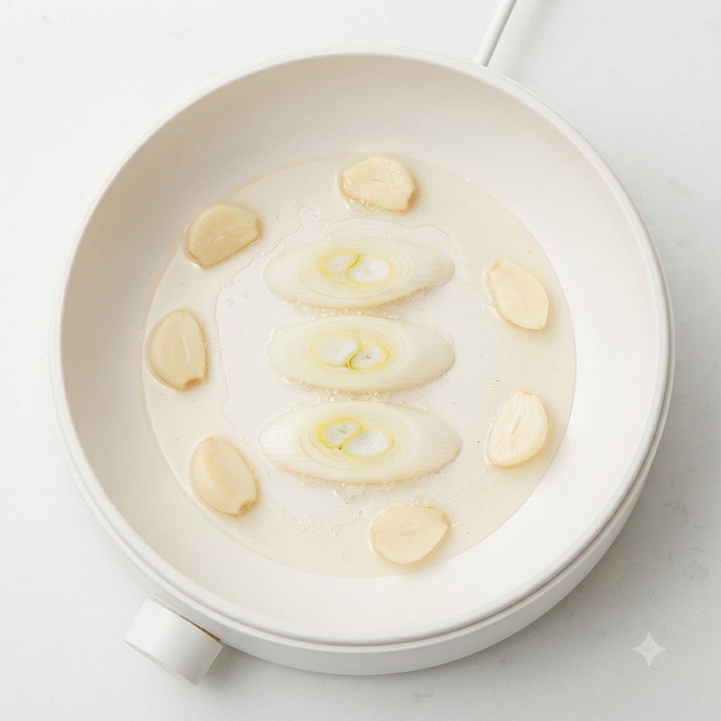 Des rondelles de cébette, des gousses dail et des morceaux de pomme de terre grésillant dans lhuile dans une marmite blanche.