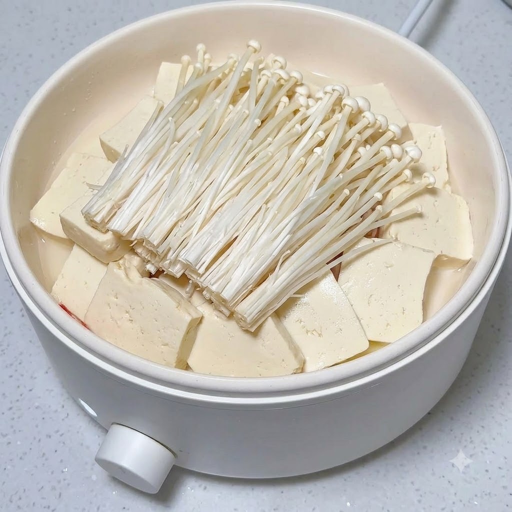 Des rondelles de piment rouge frais soigneusement disposées sur un tas de champignons enoki et de tofu dans une marmite blanche.