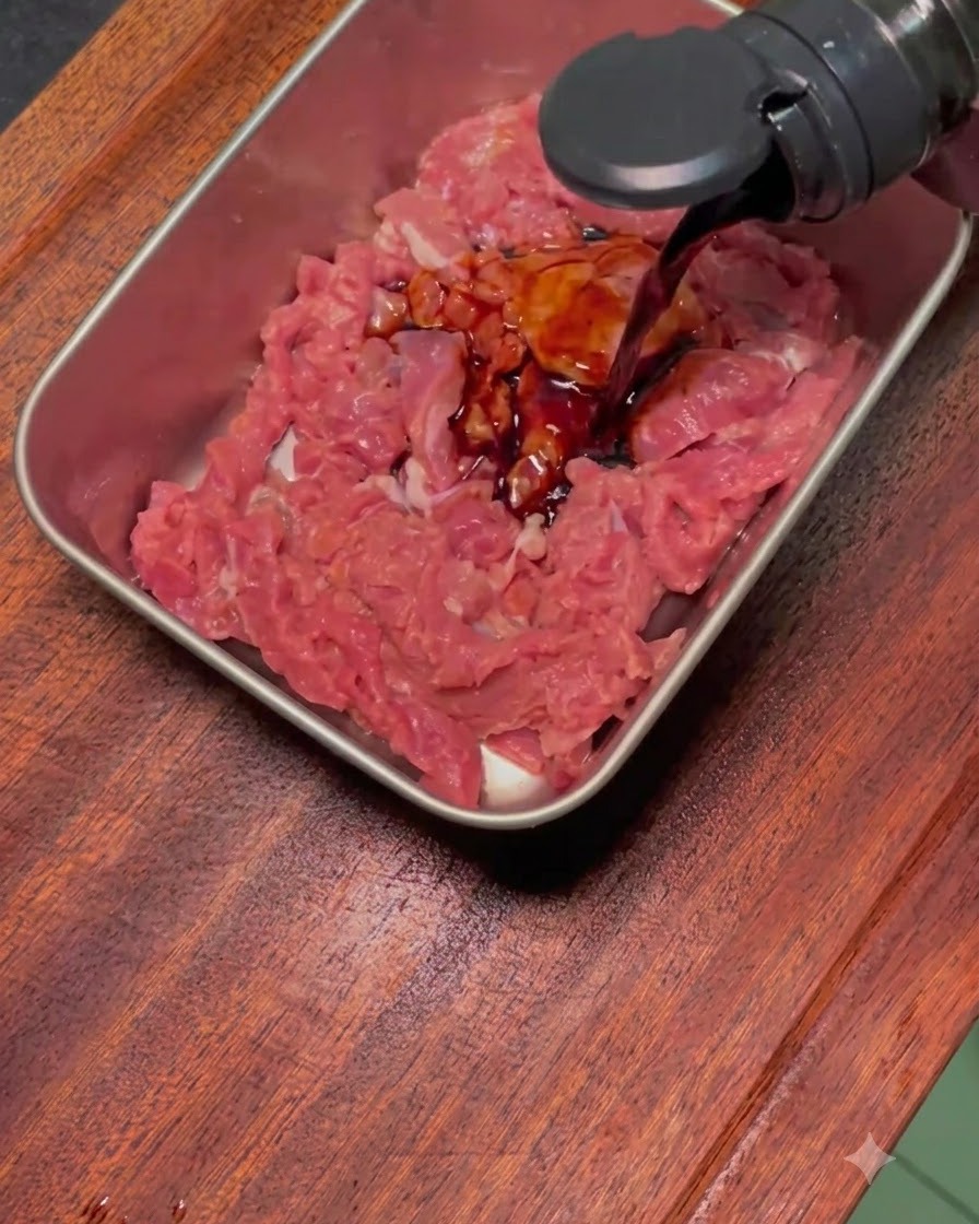 Marinade foncée versée sur des tranches de bœuf crues dans un plateau en métal.