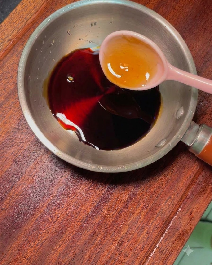 Une petite poêle en métal contenant une sauce foncée et dautres assaisonnements, avec une cuillère rose.