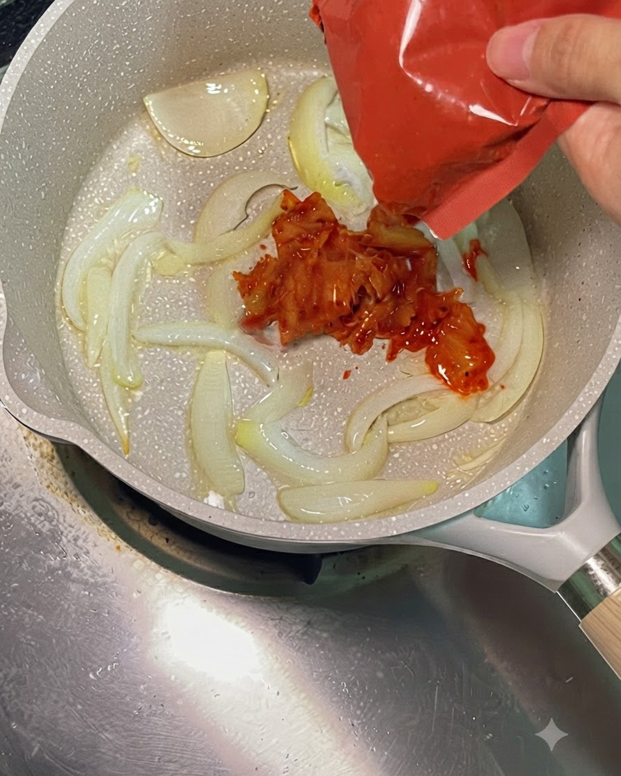Du kimchi rouge vif ajouté dans une poêle chaude avec des oignons sautés.