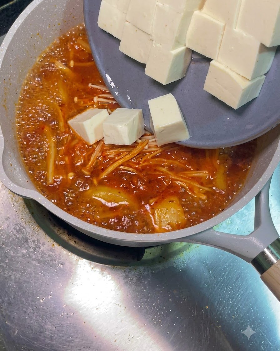 Des cubes de tofu blanc glissant dune assiette grise dans la soupe rouge bouillonnante.