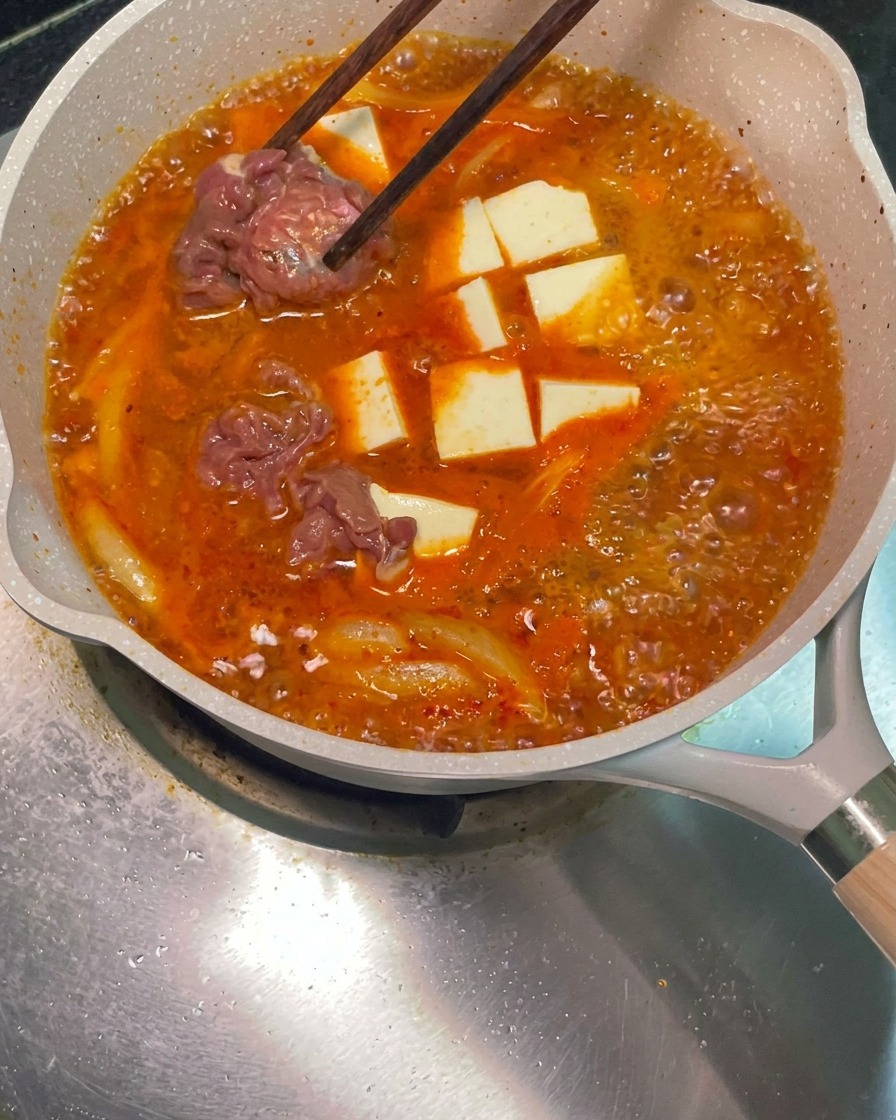 Des baguettes plaçant des tranches de bœuf crues marinées dans la soupe rouge frémissante.