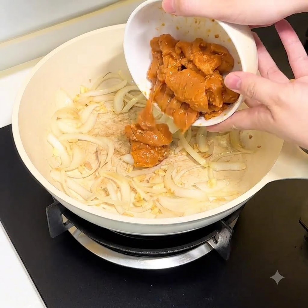 Des morceaux de poitrine de poulet versés dun bol blanc dans la poêle avec les oignons et lail.