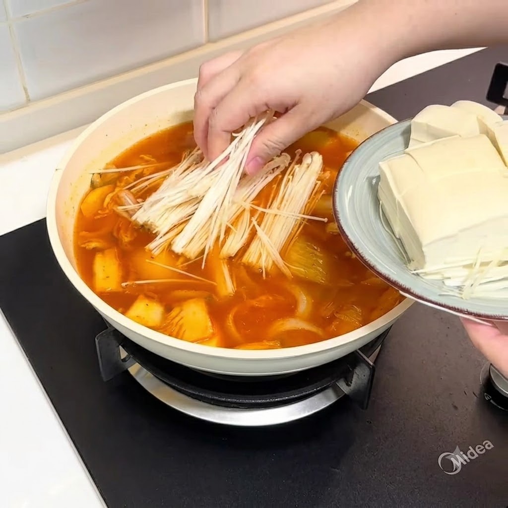Des champignons enoki et du tofu tranché ajoutés dans la casserole de bouillon.