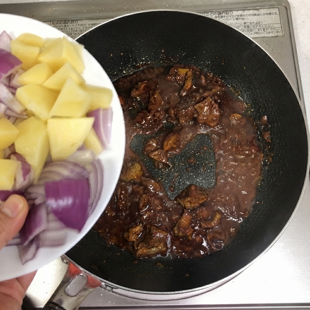 Tranches de pommes de terre et oignons rouges versés dans la poêle avec le bœuf.