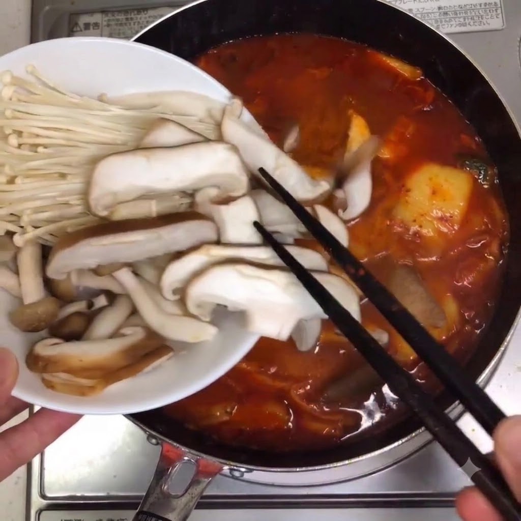 Champignons assortis et champignons enoki placés dans la casserole de soupe mijotante.